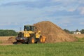 A Komatsu front end loader by a dirt pile ready for work with green grass and blue sky out in the country.