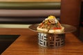 Korea Food in Restaurant on wooden table, noodles with sauteed pork vegetable on brass round circle plate with fire under