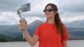 Korean blogger girl with sunglasses holds gray electronic stabilizer with phone installed. Woman traveler takes video