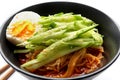 Korean cold noodles with spicy sauce, topped with cucumber, boiled egg and crushed sesame seeds in a black bowl.