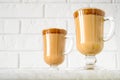 Korean Dalgona coffee in tall glass mugs. Trendy refreshment creamy whipped Macau coffee. Light brick background.