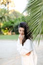 Korean dreaming girl in white sweater standing near palm leaf.