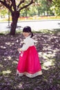 Korean girl child in a national costume walks in a garden with cherry blossoms in spring.