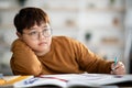 Korean schooler chubby boy dreaming about something while doing homework Royalty Free Stock Photo