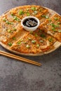 Korean style kimchi pancake Kimchijeon served with a dipping sauce and sprinkled with sesame and green onion closeup on the wooden