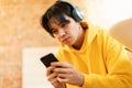 Korean Teen Boy Using Cellphone Wearing Wireless Headphones Sitting Indoors Royalty Free Stock Photo