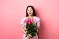 Korean teen girl in dress having romantic date on Valentines day, holding bouquet of roses and looking surprised at Royalty Free Stock Photo