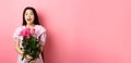 Korean teen girl in dress having romantic date on Valentines day, holding bouquet of roses and looking surprised at Royalty Free Stock Photo