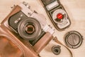 Vintage old photo-camera in leather case with exposure meter, tape cassette and lens cap on wooden background