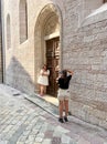 Kotor, Montenegro - 06 august 2023: Girl-photographer photographs a bride standing near the arched door of an old church