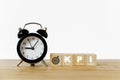 KPI, Key Performance Indicator, and dartboard icon on wooden cube with black analog alarm clock on desk