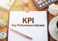 KPI short for Key Perfomance Indicator text on a clipboard with coffee, calculator, glasses, crumpled sheets and notebook