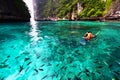 Asian man in orange life jacket with diving mask is snorkeling among many Indo-Pacific sergeant fish