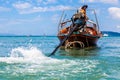 Krabi, Thailand - February 12, 2019: The driver of a longtail motorboat drives a motor with a long drive and a propeller. Sailor