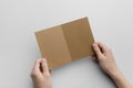 Kraft A6 Bi-Fold Half-Fold Brochure Mock-Up - Male hands holding a kraft bi-fold on a gray background