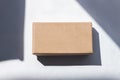 Kraft cardboard post parcel with natural sunlight shadow on white background in creative minimalism style. Eco gift box