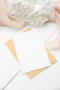 Kraft paper envelope with blank white card, peony flowers and beige cloth on white wooden table. Top view. Wedding invitation Royalty Free Stock Photo