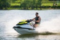 BRP Sea-Doo jet ski watercraft driver in goggles drives water bike at high speed splashing at sunset by river bank. Active summer