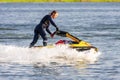 Young Caucasian jet ski woman drives standing on watercraft making splashes at sunset by river bank at countryside. Beautiful