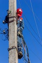 A male electrician on a pole mounts a line of electrical wires against the blue sky close up