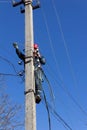 A male electrician on a pole mounts a line of electrical wires on a blue sky background close up Royalty Free Stock Photo