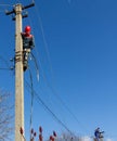 Male electricians on poles mount a new line of electrical wires against a blue sky with a copy space Royalty Free Stock Photo