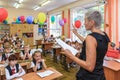 First-form schoolchildren in classroom at school desks on holiday of beginning of elementary school education. Woman teacher runs