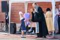 Orthodox Christain priest blessing schoolgirl on holiday of beginning of elementary school education. Girl gives flowers to priest