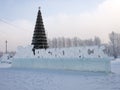 The name of the city in Russian carved out of ice stands against the background of a Christmas tree decorated.