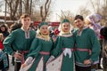 Young people in Russian ethnic costumes pose against the backdrop of a crowd of people at the Farewell to Winter holiday in a city