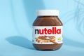 Nutella in a glass jar on a blue background with hard shadows from sunlight.