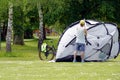 A man setting up a tent in a park. There is bike behind the tent.