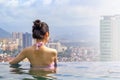 Beautiful girl in the pool on the roof of the building admires the views of the city