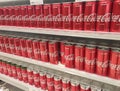 Soft drinks in cans are displayed on a shelf for sale in a large supermarket.