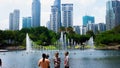 Unidentified tourist at KLCC Park with a water fountain show and tall skyscraper building at the background during the day.