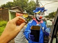 Kudus - Indonesia, February 11 2022: Badut Jalanan is a beggar dress up in funny clown a stop of red traffic light in Indonesia