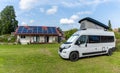 Gray camper van parked at a campground with a sanitary facilities building with solar panels behind