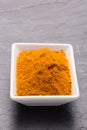 Kurkuma spice powder in white bowl on dark slate background.