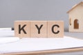 KYC text made of wooden blocks on gray background with a small wooden model house