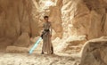 Cosplayer girl portrays character Rey Skywalker from the Star Wars universe with lightsaber in her hand among sandy canyon