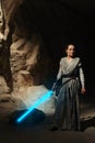 Cosplayer girl portrays character Rey Skywalker from the Star Wars universe with lightsaber in her hand among sandy canyon