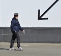 A man wearing a mask and goggles walks past a black arrow pointing downwards