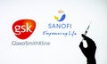 Kyiv, Ukraine - December 22, 2020: Backlit single shot image of Sanofi and GSK logo on tv screen with a hand holding an Covid-19