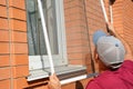 Man installing mosquito net, mosquito wire screen on brick house window outdoors Royalty Free Stock Photo