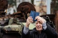 Elderly man taking a selfie near a burnt and melted rusty wreckage of a Soviet Russian-made tank Royalty Free Stock Photo