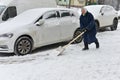 An elderly woman cleans the sidewalk from snow