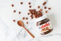 KYIV, UKRAINE - February 21: Nutella chocolate hazelnut spread in a glass jar with white cap next to wooden spoon and raw