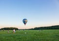 Hot air balloon in clear sky over field with people. Colorful balloon on aerial landscape background. Summer leisure. Royalty Free Stock Photo