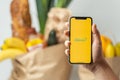 KYIV, UKRAINE - January 17: Female hand holds mobile phone with Glovo logo on yellow screen against products from grocery store.