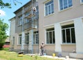 Building contractors on scaffoldings are renovating the facade of a school building, painting the